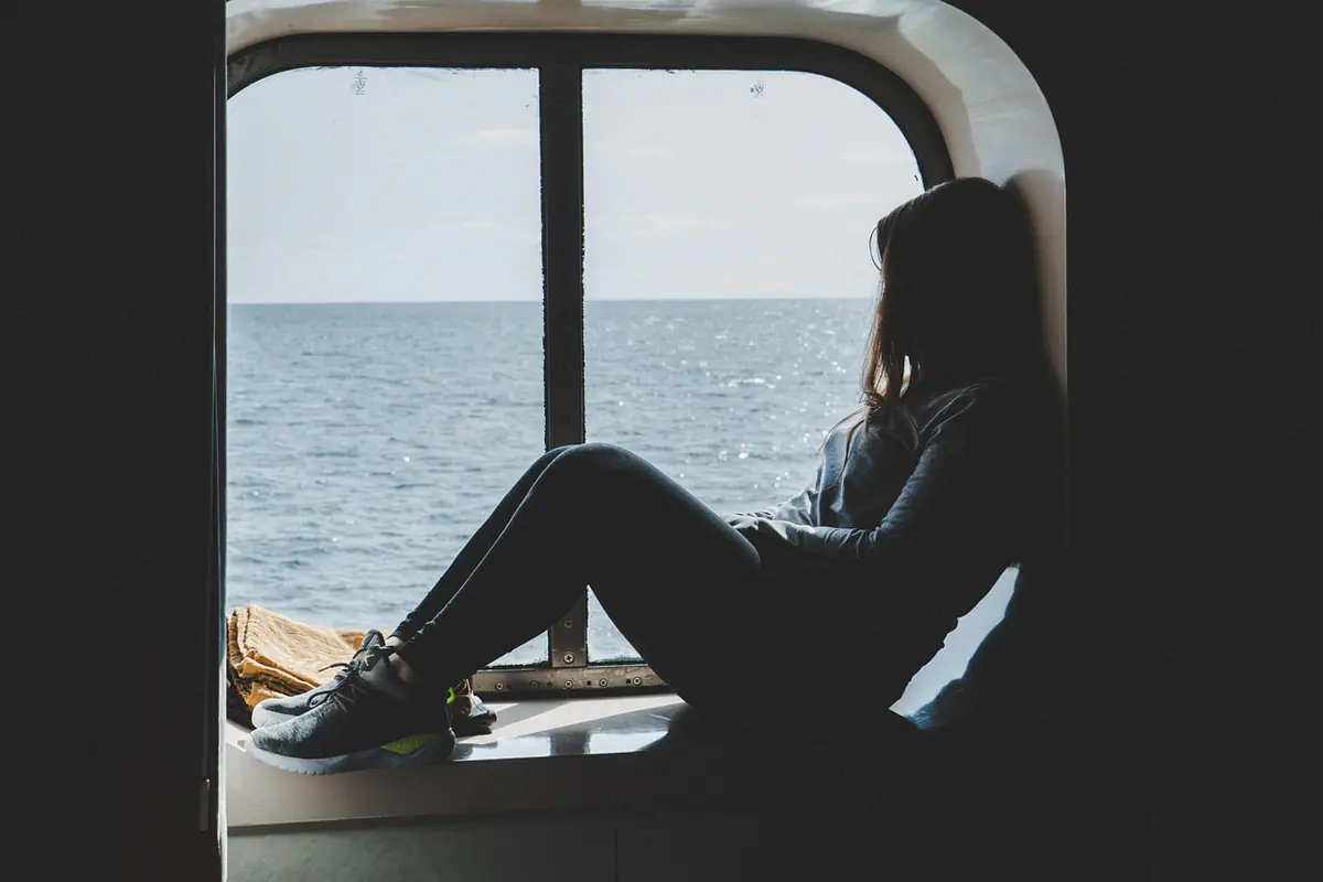 Silueta de una mujer sentada junto a una ventana con vista al mar