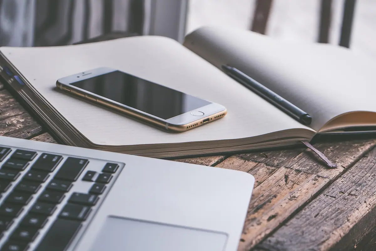 Computadora portátil, teléfono y libreta sobre un escritorio de trabajo