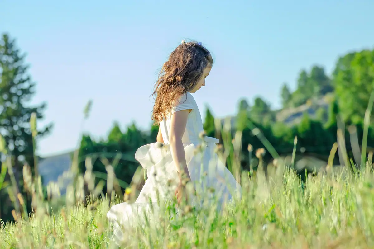 Niña con vestido blanco de comunión posando en un campo