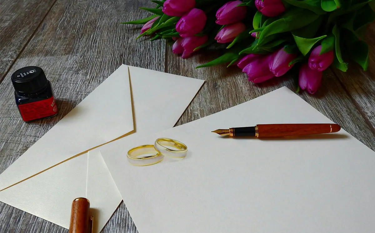 Anillos, flores, sobre y papel preparados para una invitación de boda