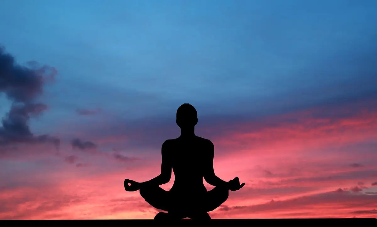 Silueta de una mujer sentada en postura de meditación al atardecer