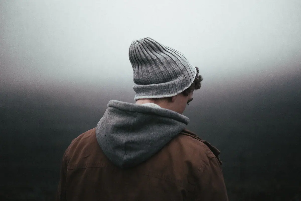 Hombre de espaldas con gorro frente a un paisaje con niebla