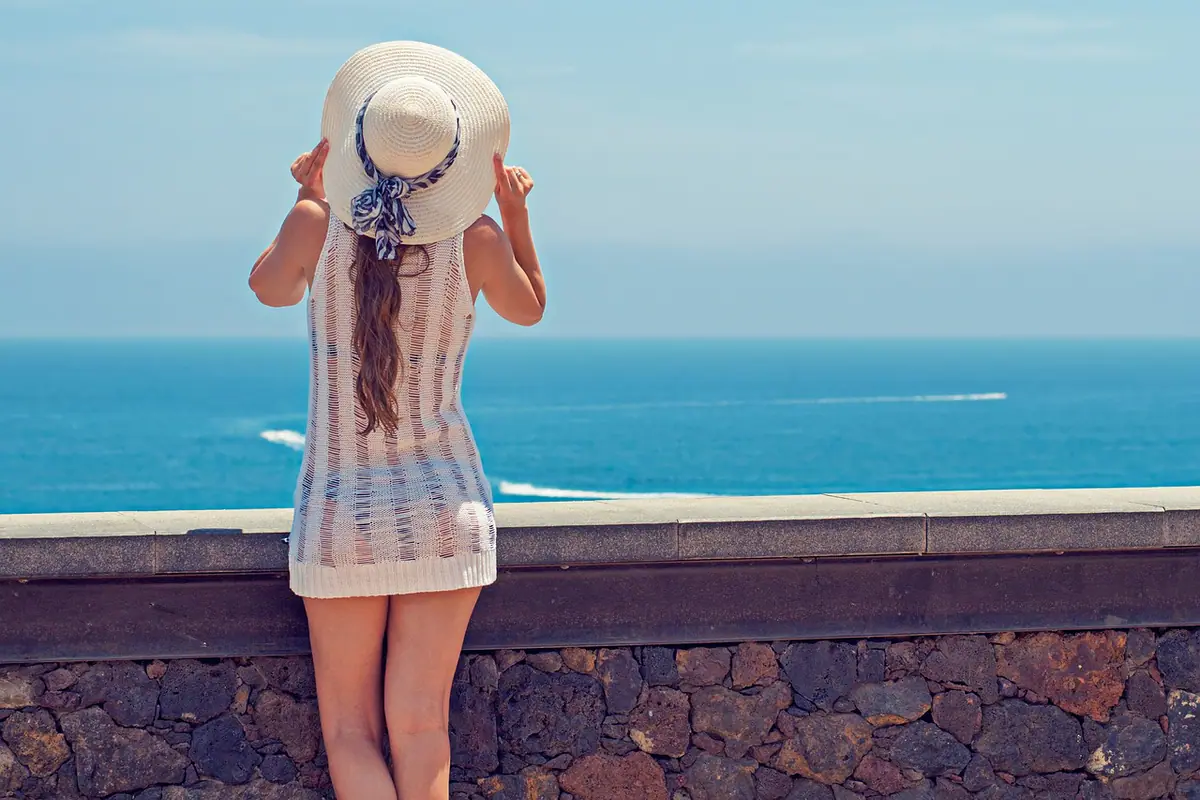 Mujer con sombrero vista de espaldas frente al mar