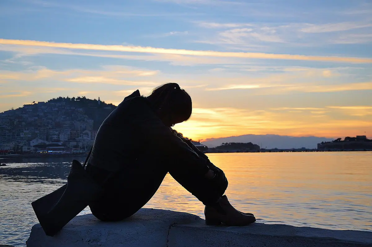Silueta de una mujer sentada frente al mar al atardecer