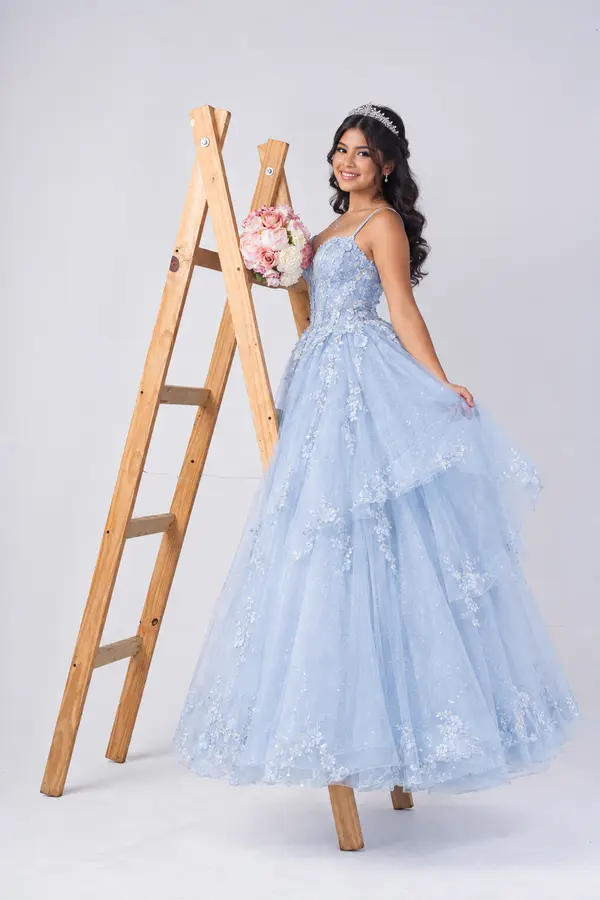 Quinceañera con vestido largo apoyada en una escalera, cuerpo completo
